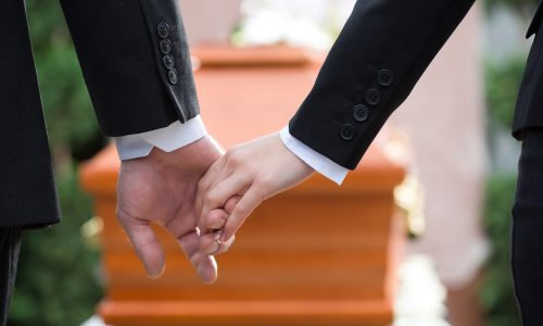 Religion, death and dolor - couple at funeral holding hands consoling each other in view of the loss